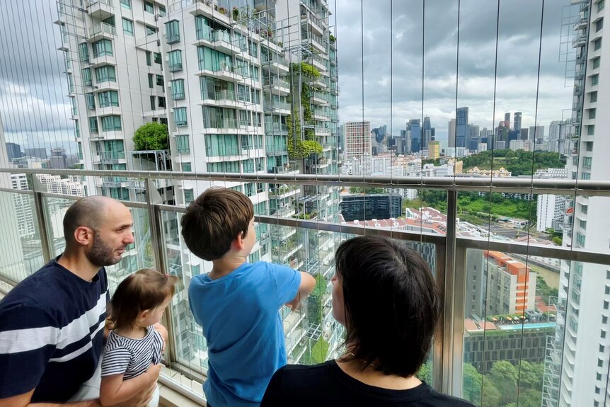 A man, woman and two children looking out from an apartment balcony in Singapore at other apartment buildings around them.