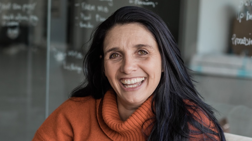 Olympia Yarger wearing a tan jumper laughs toward the camera