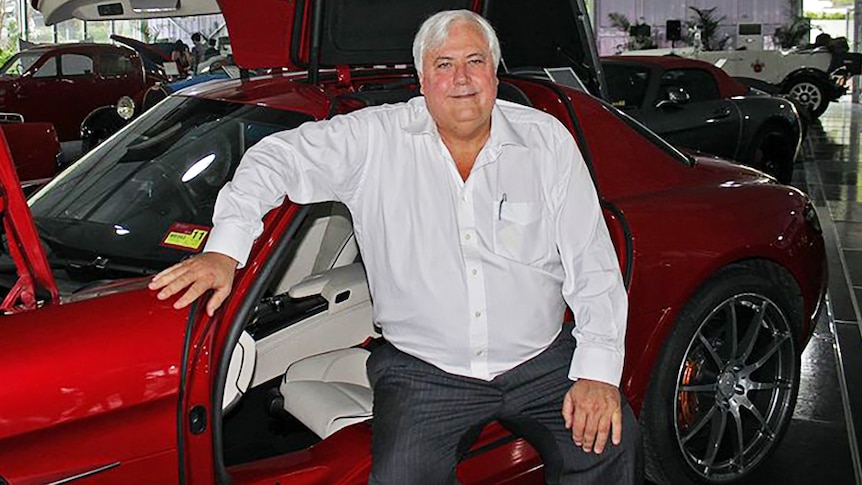 Clive Palmer sits beside a red sports car inside his motoring museum
