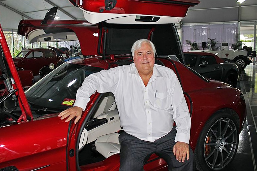 Clive Palmer sits beside a red sports car inside his motoring museum