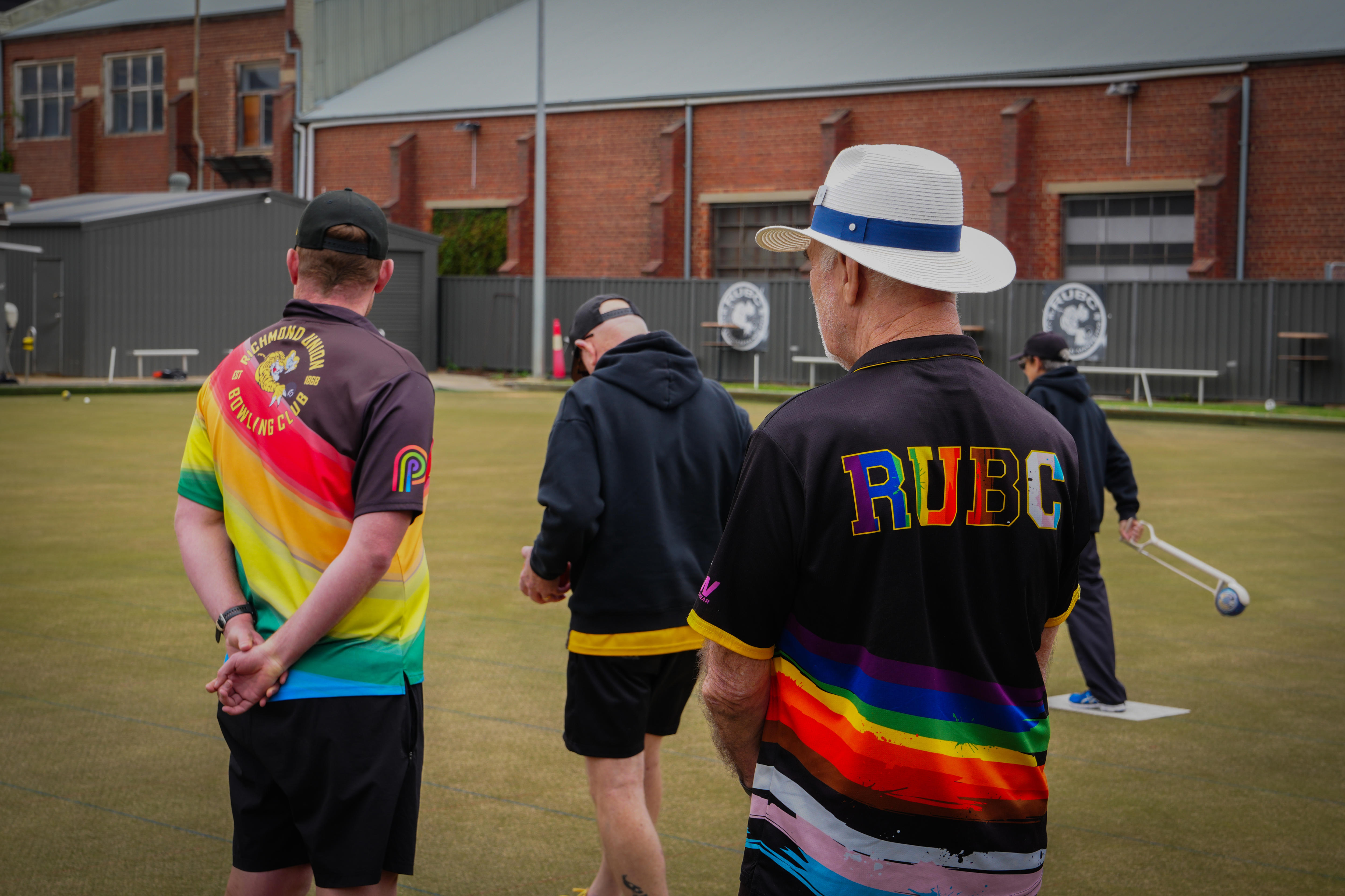 Quatro jogadores de boliche observam o gramado enquanto um participante se prepara para jogar.