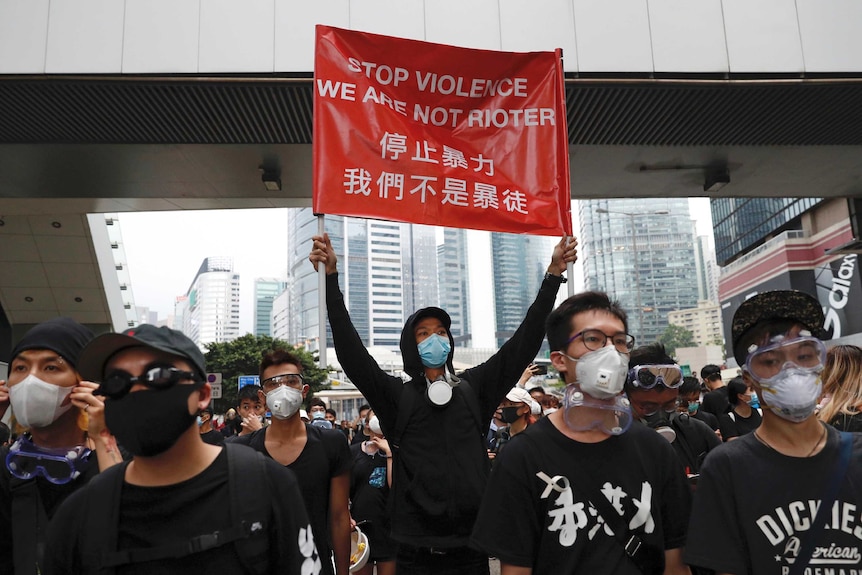 a group of men wear coverings over their mouths and noses, one holds up a sign saying stop violence we are not rioter