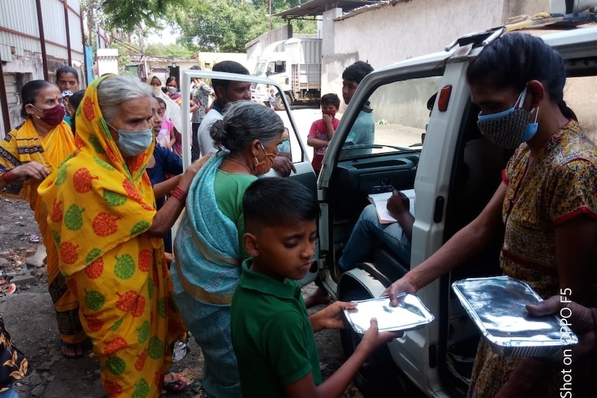 A woman handing an out food packages to a child and vulnerable woman in India.