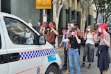 Protesters block a police van with red paint on their hands.