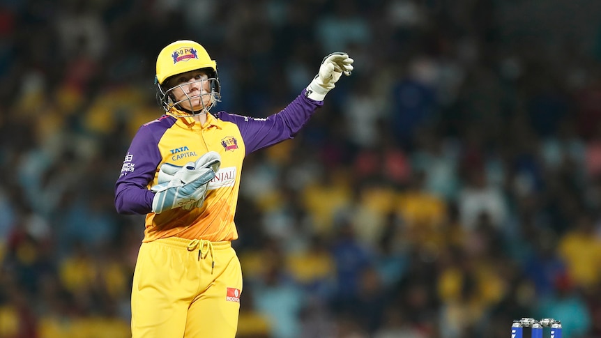 UP Warriorz wicketkeeper Alyssa Healy stands on the field with one glove on during a WPL match against Mumbai Indians.