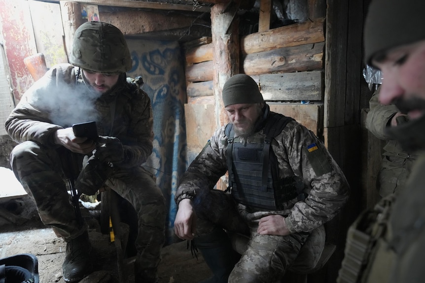 Several men in military camouflage uniforms hang out in a bunker. 