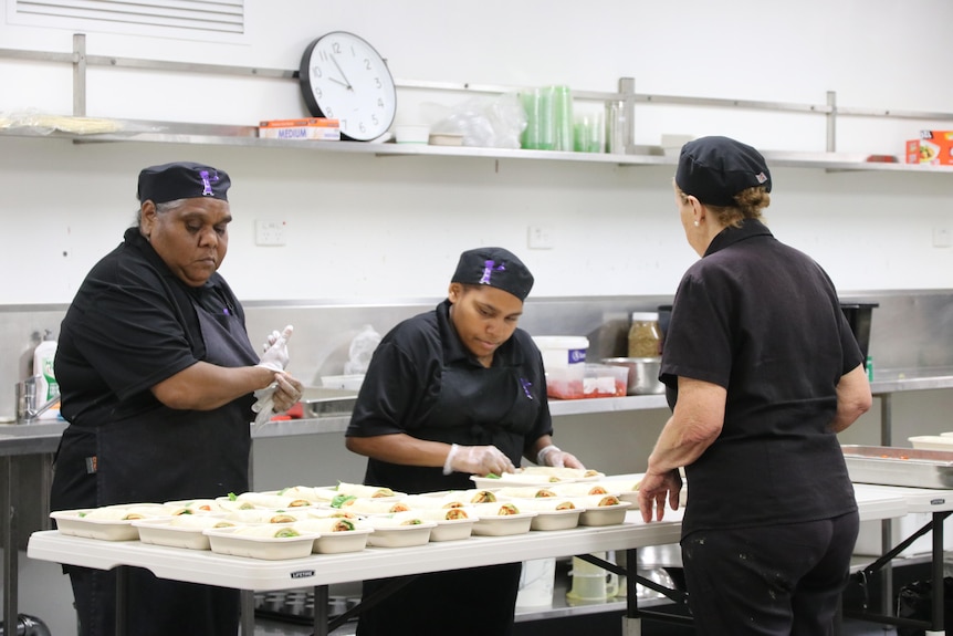 Three women serving food in an industrial kitchen