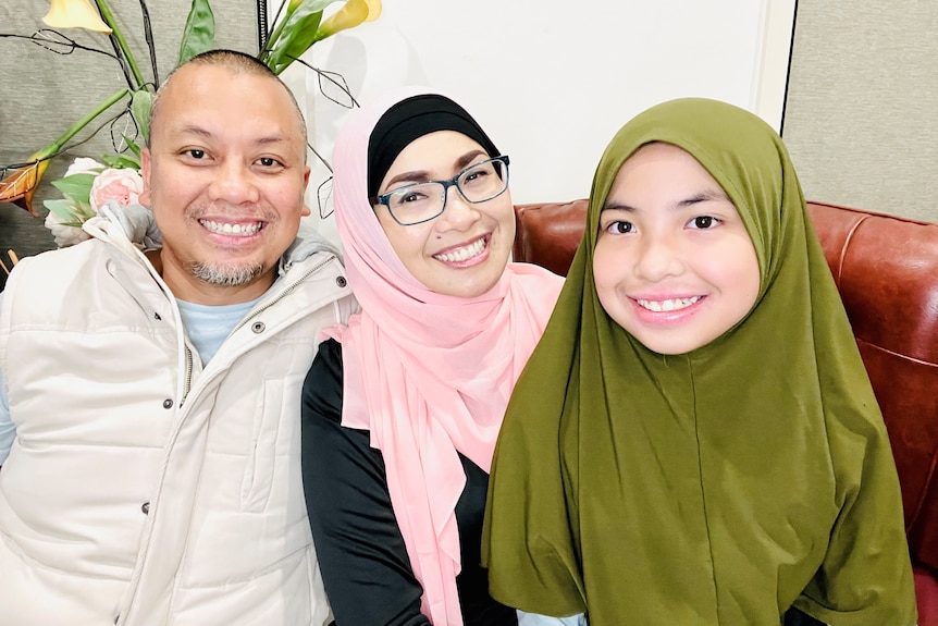 A family of three sitting on a couch together and smiling to camera