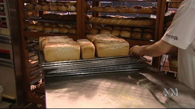 Hands stack bread on a rack in a bakery