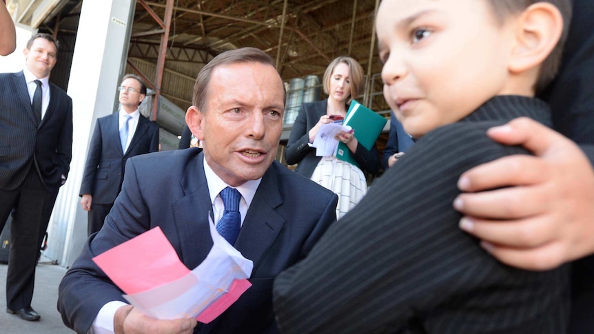 Tony Abbott receives a paper aeroplane from five-year-old Denzil Hammam