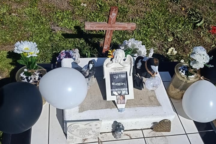 A grave with black and white balloons and a sign for maggies. 