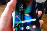 A hand holds a half-folded Samsung Galaxy Fold phone out in front