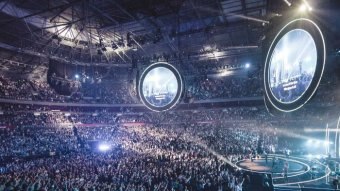 A stadium filled with people raising their hands and dancing while a group of people stand on stage.