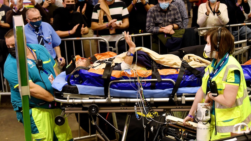 A male cyclist is taken from a velodrome on a stretcher, assisted by medical staff.