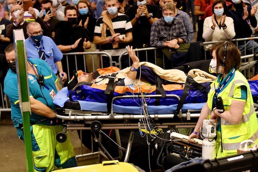 A male cyclist is taken from a velodrome on a stretcher, assisted by medical staff.