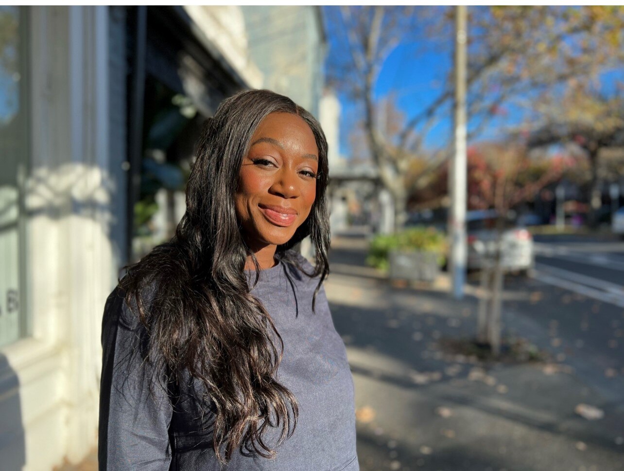 Jill Dzadey looks to the camera with a smile on her face while standing in a Carlton Street on a sunny day.