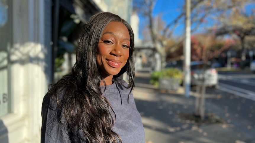 Jill Dzadey looks to the camera with a smile on her face while standing in a Carlton Street on a sunny day.