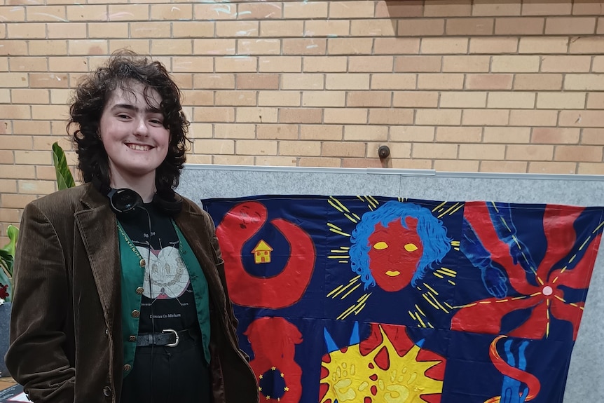 A person with dark curly hair standing in front of a blue and red quilt