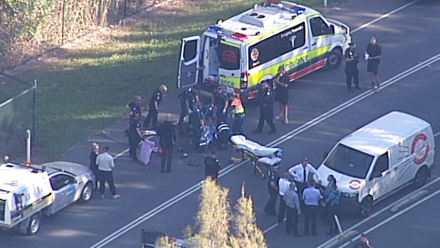 Paramedics and police and their vehicles on a road surrounding an injured man