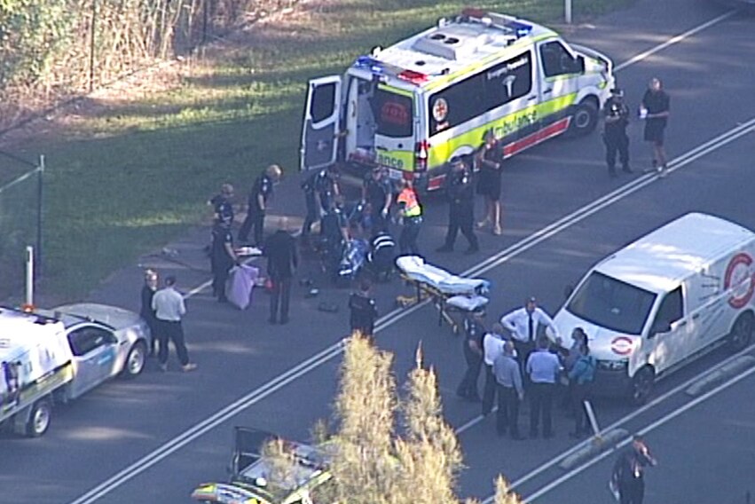 Paramedics and police and their vehicles on a road surrounding an injured man