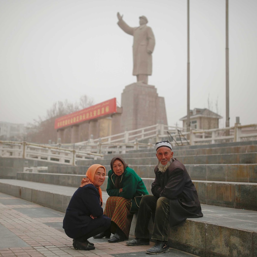 Ethnic Uighurs sit near a statue of China's late Chairman Mao Zedong.
