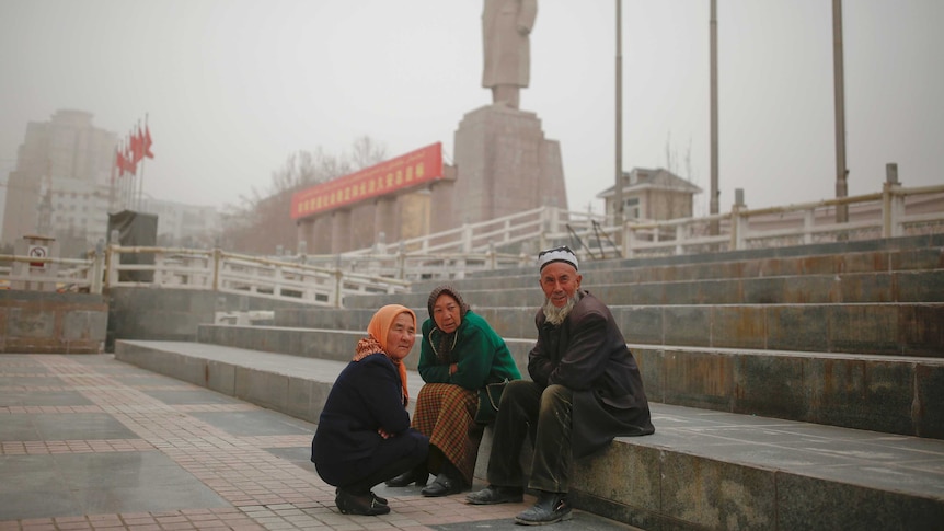 Ethnic Uighurs sit near a statue of China's late Chairman Mao Zedong.