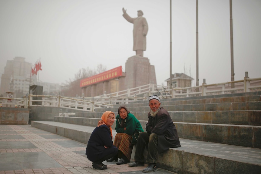 Ethnic Uighurs sit near a statue of China's late Chairman Mao Zedong.