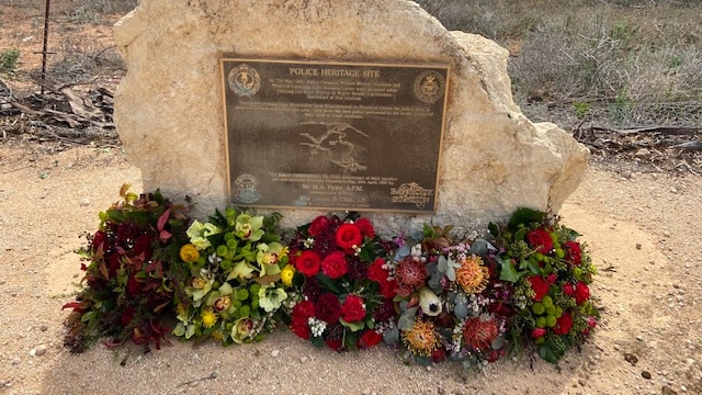 A memorial plaque to fallen police officers cast into a white rock, with fresh flower bouquets laid at its feet.