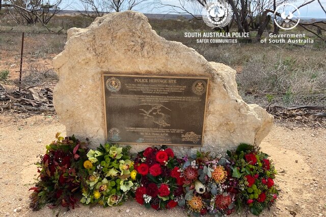 A memorial plaque to fallen police officers cast into a white rock, with fresh flower bouquets laid at its feet.