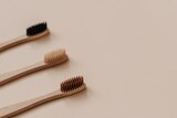 Three eco looking toothbrushes lay upon a beige background. 