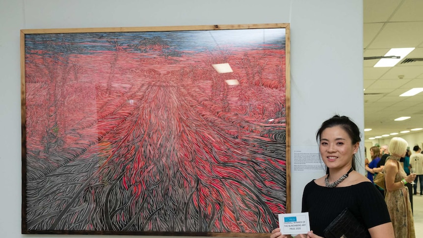 A woman dressed in black stands next to her award-winning artwork.