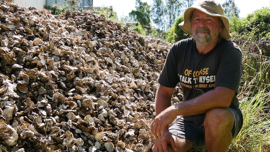 A man crouching down in front of a big pile of oyster shells