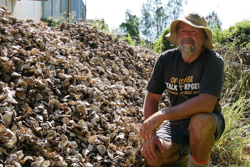 A man crouching down in front of a big pile of oyster shells