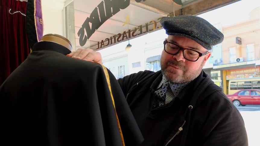 Tailor Rhyce Winterbourne in the window of his Sydney shop measuring a cassock (religious robe).