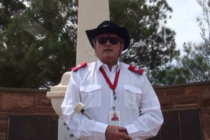 A man in a white long-sleeve shirt, a black hat and black sunglasses stands proudly.