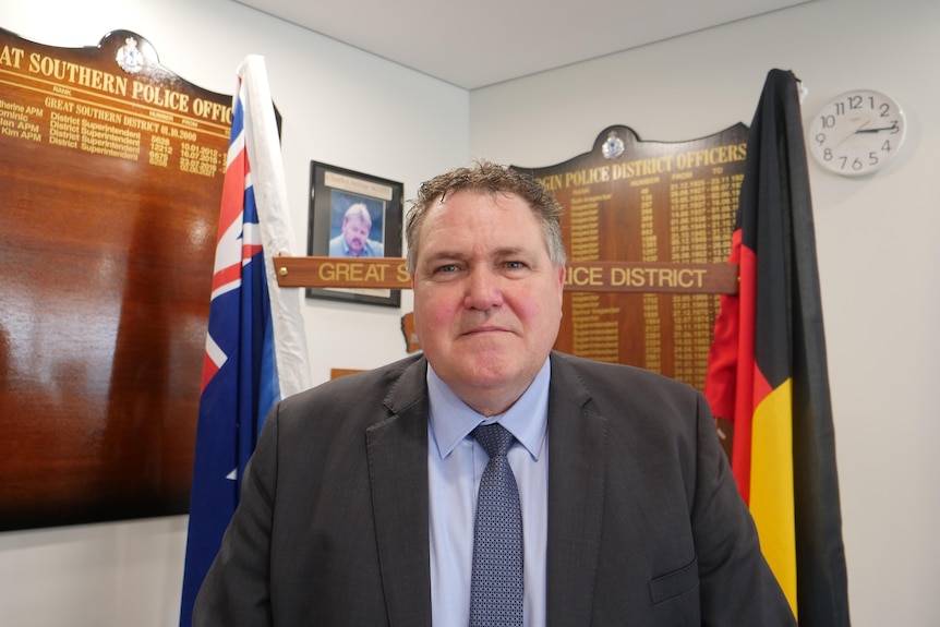 Albany Detective Senior Sergeant Darryl Noye stands in front of the Australian and Aboriginal flags