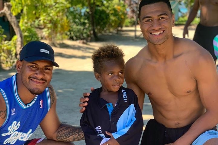 A shirtless Ronaldo Mulitalo smiles while putting his arm around a small child