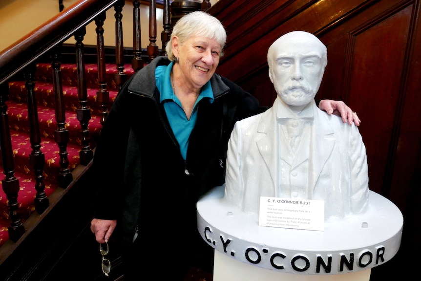 A woman with her arm around the sculpture of a man with a mustache. 