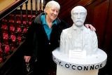 A woman with her arm around the sculpture of a man with a mustache. 