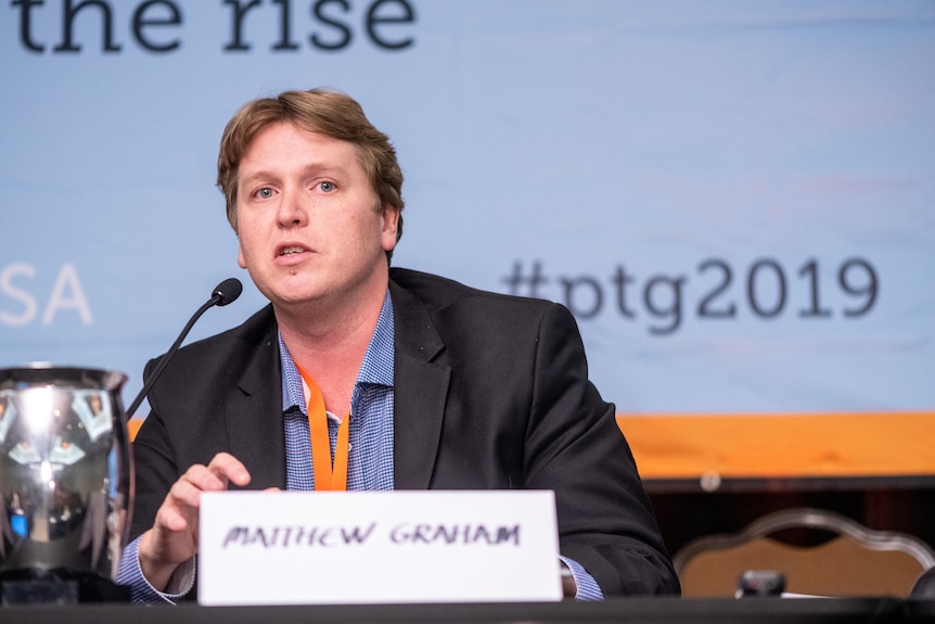 Matt Graham sits in front of a microphone and a name card.