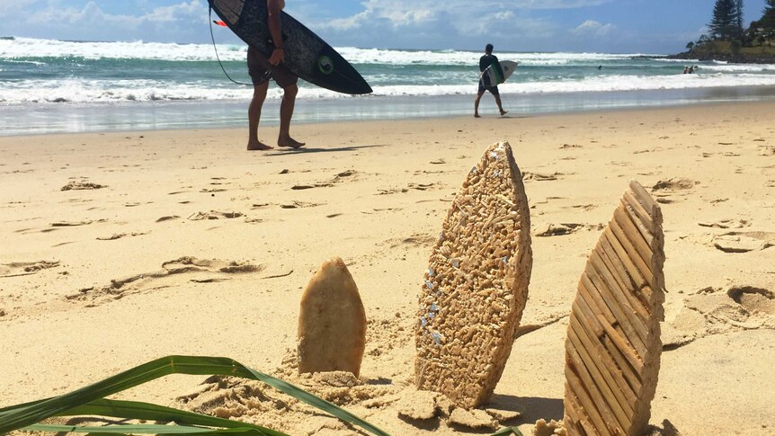 Small lemongrass surfboard prototypes sit in beach sand