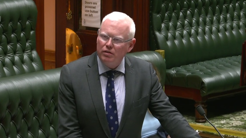 A man in a dark suit speaks in parliament.