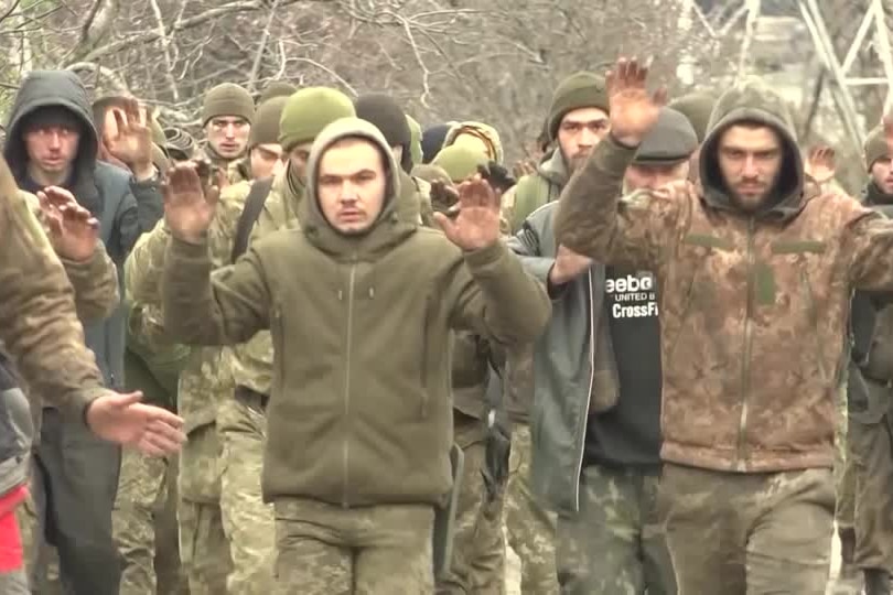 A group of men in camaflouge walk with their hands in the air