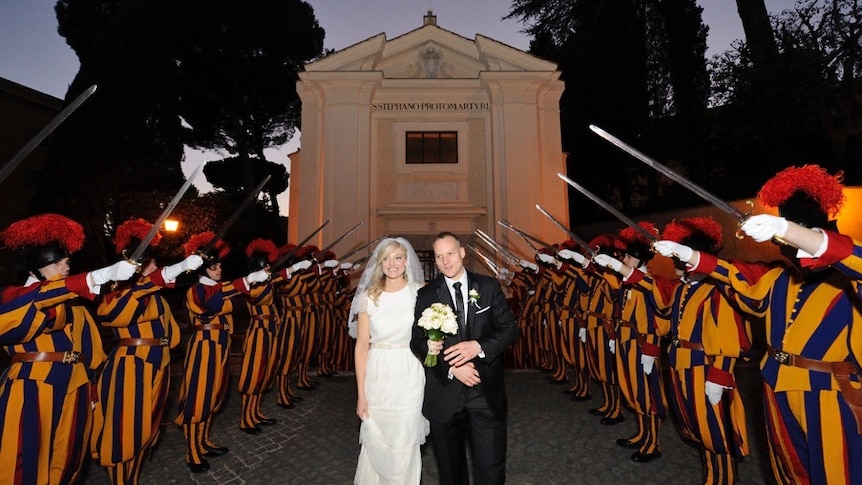 Bridal couple walking along path flanked on both sides by swiss guards in full uniform with swords raised in the air