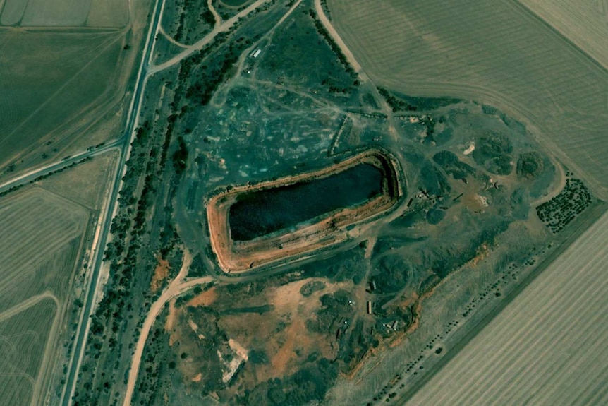 Satellite image of the dam with water in it and green fields around about it.