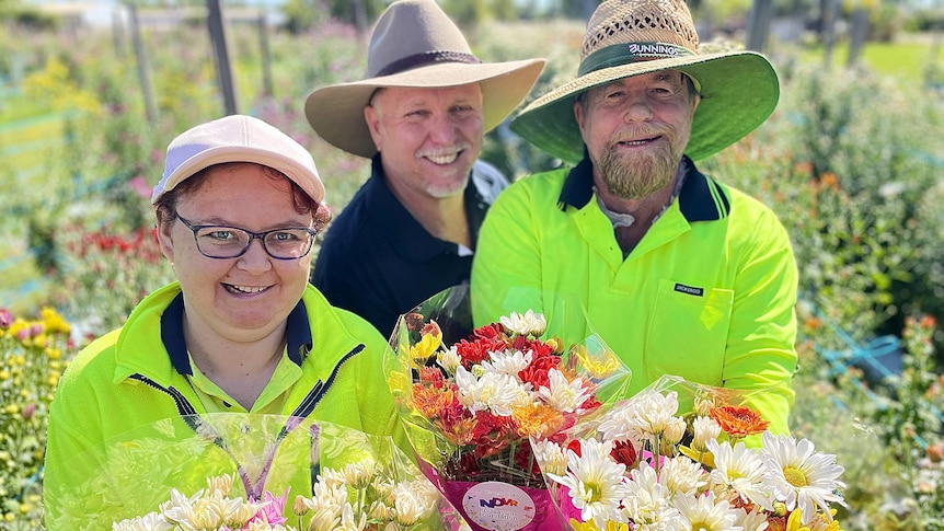 Three people wearing wide-brimmed hats hold colourful bunches of flowers 