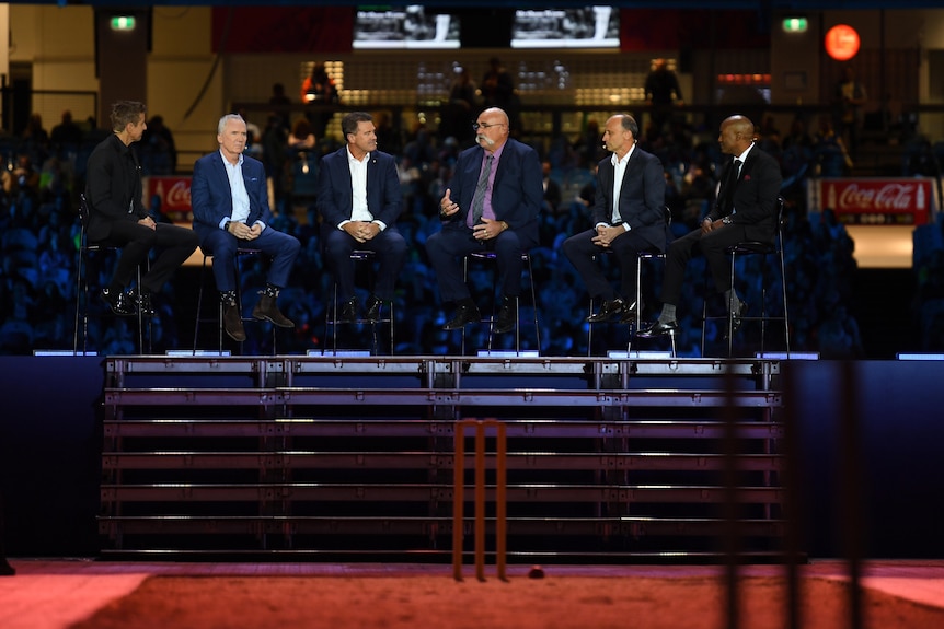 A group of men wearing suits seated on stage as part of a panel.
