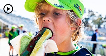 Young boy bites into a sausage in bread.