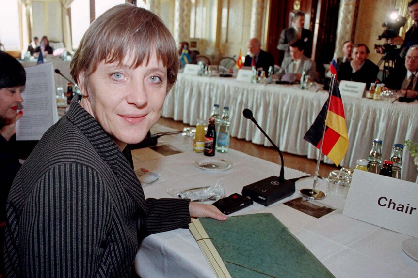 Angela Merkel turns and smiles at the camera during a conference.