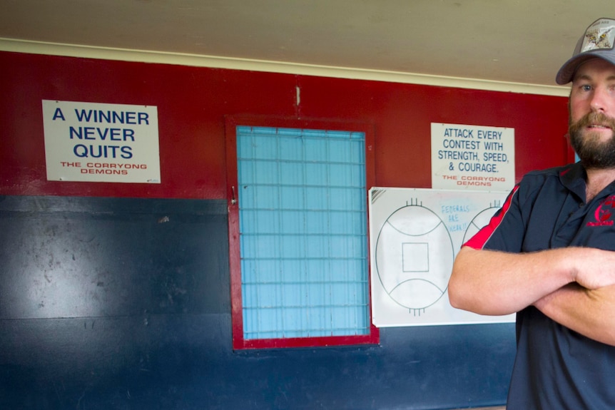 A football club coach folds his arms inside the team change rooms.